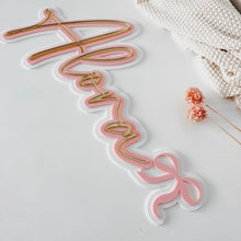 Load image into Gallery viewer, A pink and gold script name sign spelling 'Amanda' on a white surface, styled with a cream knit blanket and small dried flowers.
