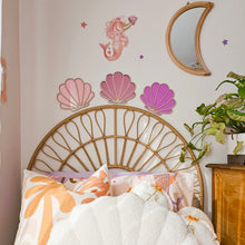 Load image into Gallery viewer, A cozy bedroom scene featuring a large white shell-shaped plush pillow on a pink and white patterned bedspread, styled with matching seashell wall decals and a wicker headboard.
