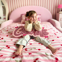 Load image into Gallery viewer, A young girl sits on a pink bed with a cherry-patterned duvet, holding a large decorative sign that says 'Charlotte'. The room has pink and white striped wallpaper and matching pink bedding.
